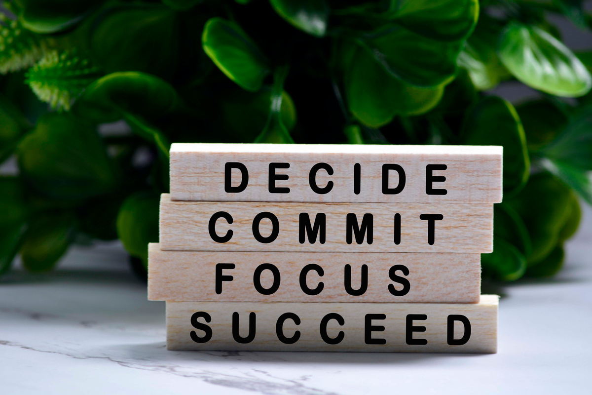 Inspirational words of decide commit focus succeed on wooden blocks with green background